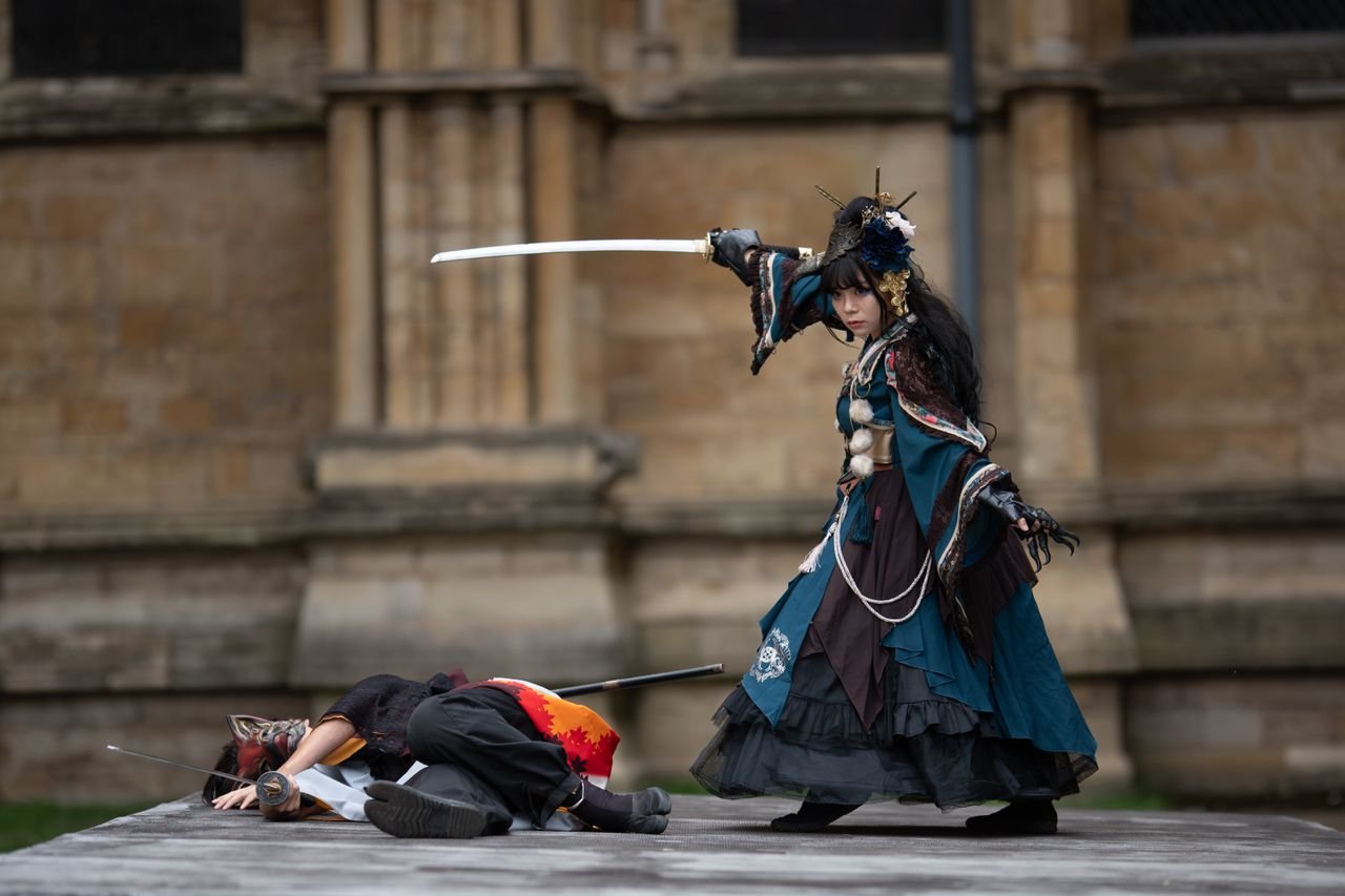 Dramatic outdoor cosplay scene with sword fight and elaborate costumes.